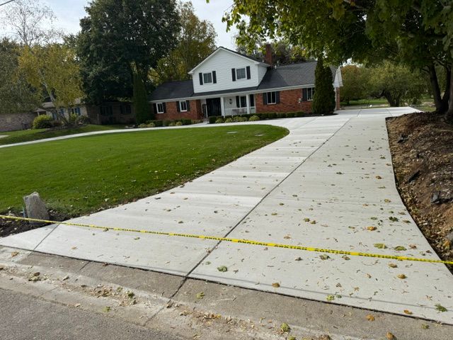 Long concrete driveway to a white house with a large green lawn and autumn leaves.