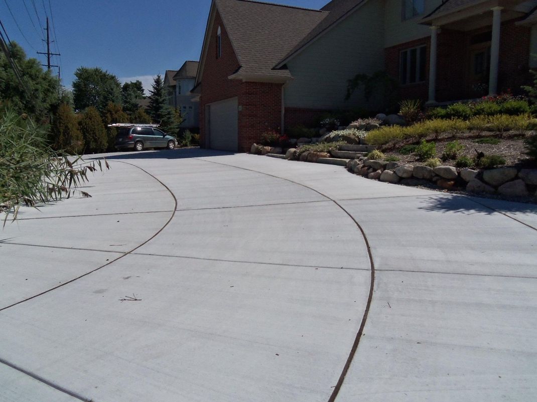 Curved concrete driveway beside a house and landscaped yard on a sunny day
