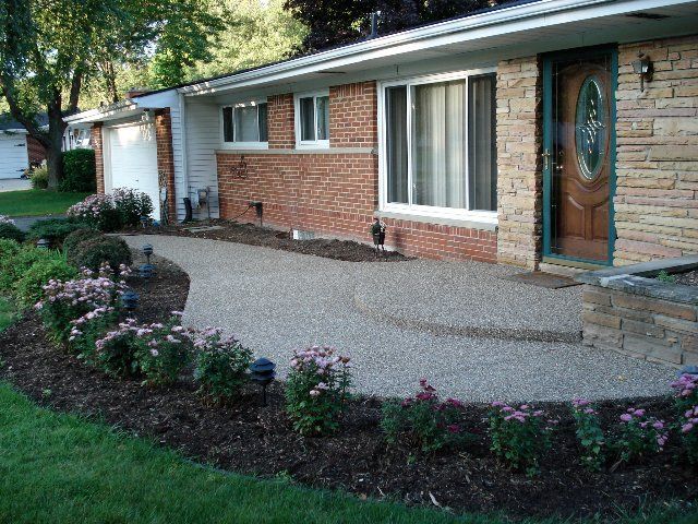 Brick house with curved concrete walkway, front flower beds, and a wooden front door