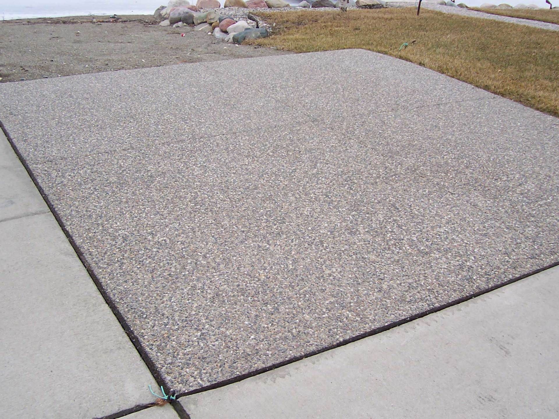 Concrete sidewalk with a large gravel patch next to a curb and grassy edge