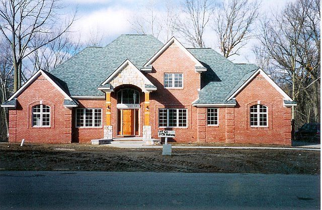 Brick suburban house with green roof and arched front entrance, surrounded by leafless trees.