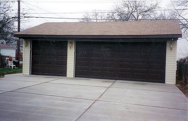 Two-door detached garage with a concrete driveway and brown roof under an overcast sky