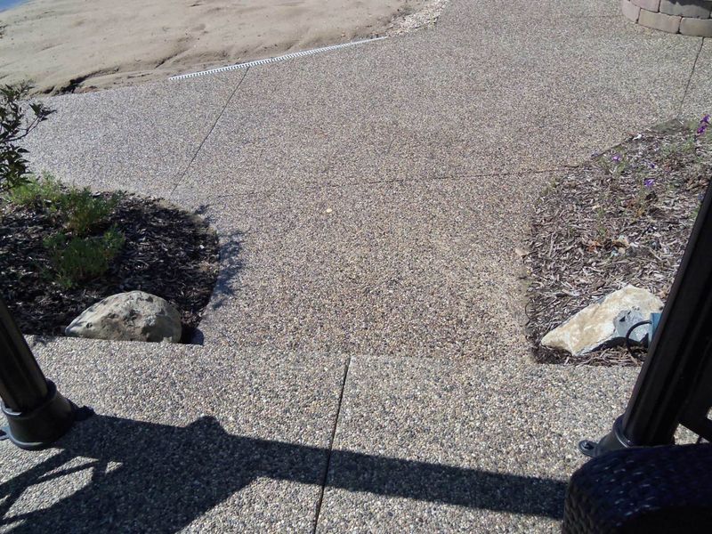 Stone walkway with damaged edges and rocks, viewed from a porch or steps.