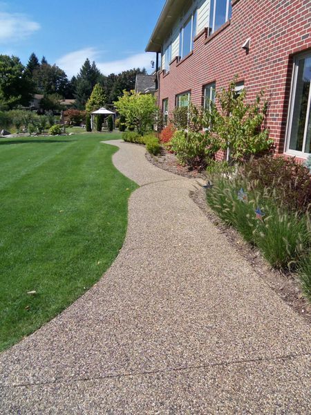 Curved gravel path beside a brick house and manicured green lawn in a sunny garden