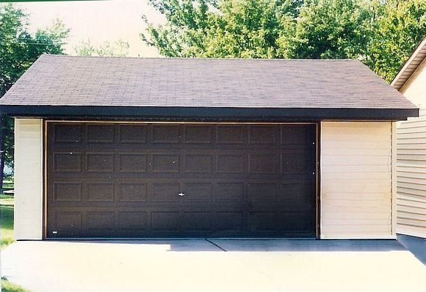 Small detached garage with a dark double door and beige siding, viewed from the front.