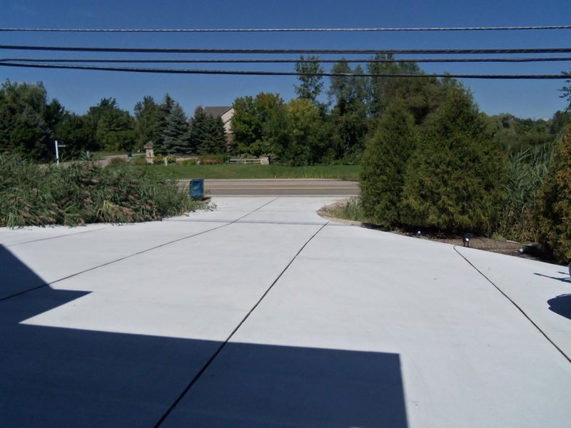 Driveway with bright white concrete, bordered by bushes and trees under a clear blue sky