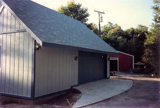 Gray building with dark roof and curved concrete walkway beside trees
