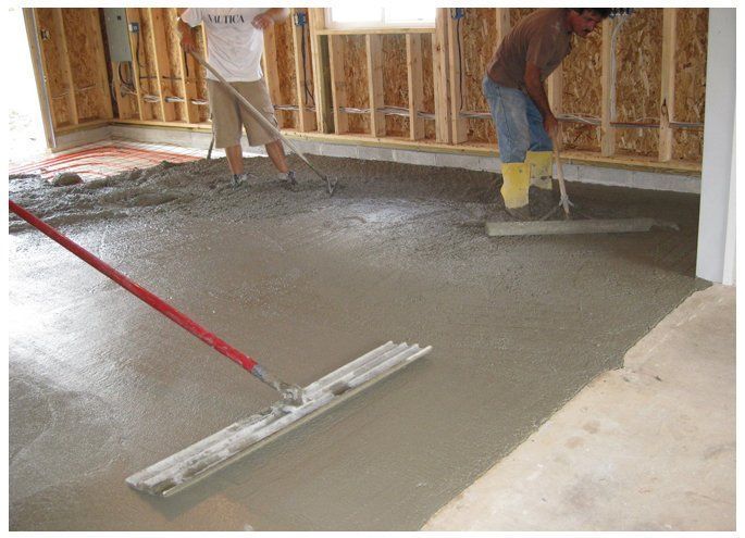 Workers leveling wet concrete inside a room under construction