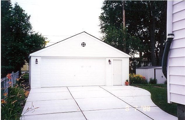 Detached white garage with a double door and driveway in front, surrounded by trees and a house on the right