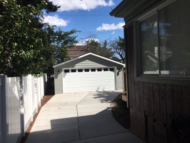 White two-car garage with a sloped driveway, framed by trees and shrubs.