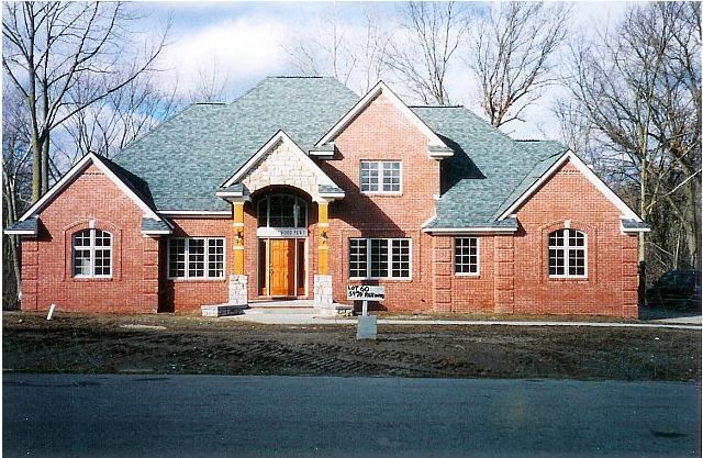 Brick suburban house with green roof and front porch, set among leafless trees