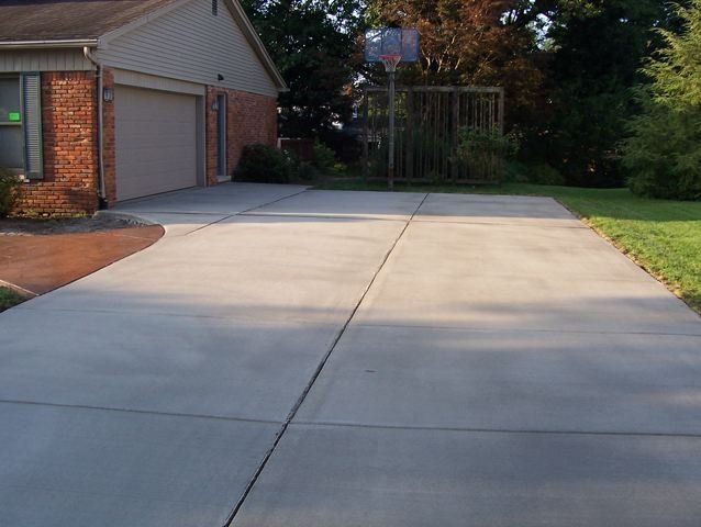 Empty concrete driveway beside a brick house, with a garage and grassy yard at the end.