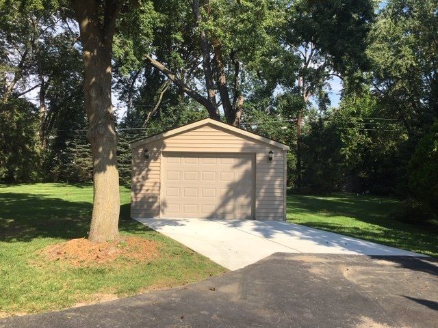 Tan garage beside a driveway, surrounded by trees and lawn