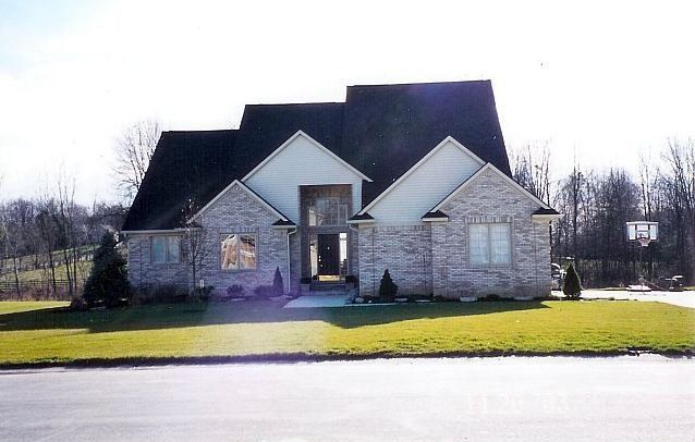Suburban house with gray stone exterior, dark roof, and bright green lawn in daylight