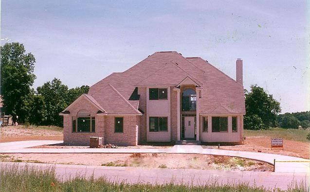 Partially built house with exposed roof framing and unfinished brick exterior on a dirt lot