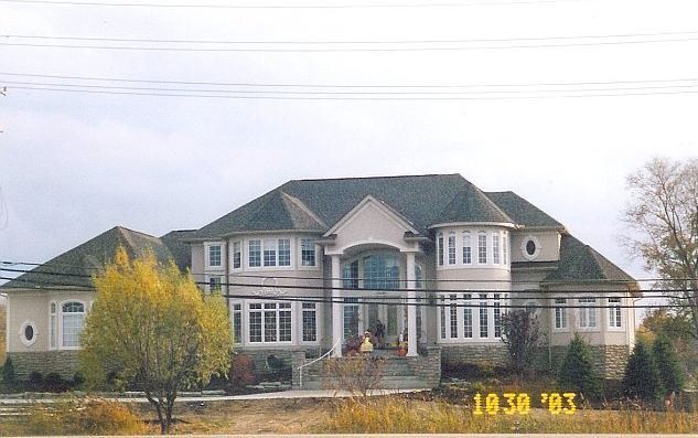 Large gray two-story house with a gabled roof and autumn trees in front