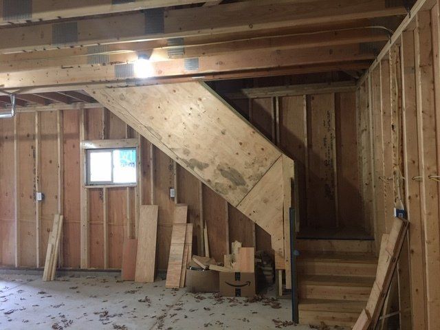 Unfinished basement with exposed studs, staircase, and small window under wood beams