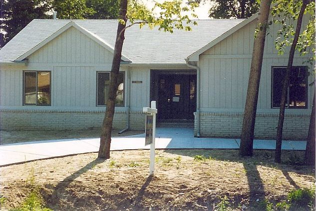 Small light-blue house with a front walkway, porch, and trees in the yard.