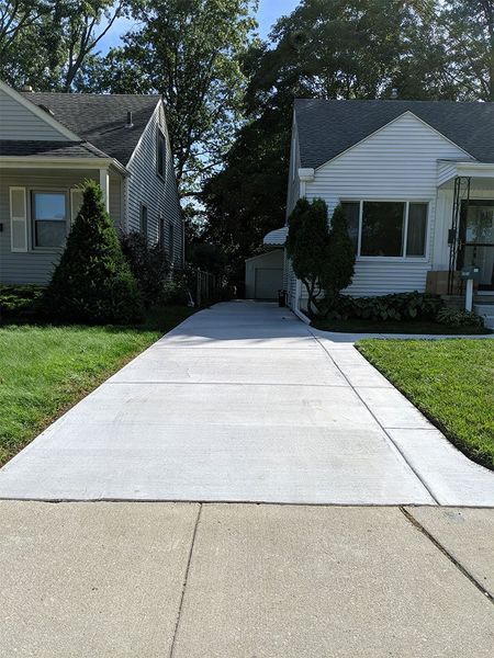 Driveway between two houses leading to a small backyard gate on a sunny day.