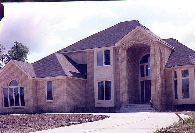 Suburban brick house with a sloped roof, arched front entry, and a concrete driveway under a cloudy sky