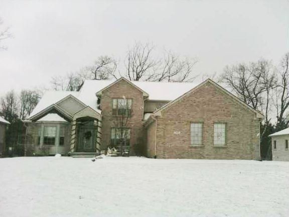 Snow-covered suburban house with brick and beige siding in a winter yard
