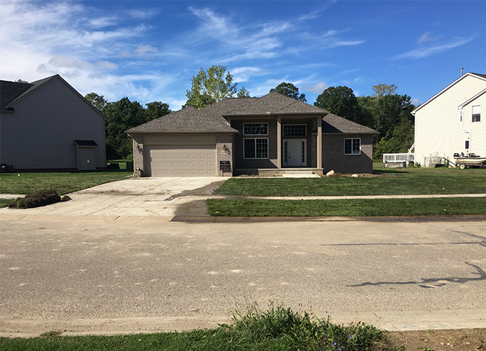 Single-story brick house with a two-car garage and driveway on a suburban street under a blue sky