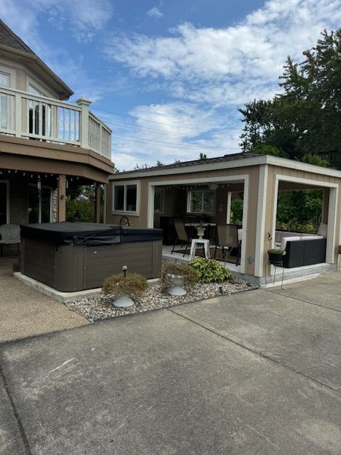 Backyard patio with hot tub, lounge chairs, and a small covered seating area beside a house