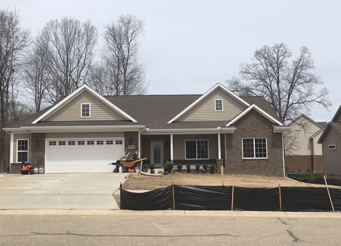 Single-story house with attached garage, stone facade, and unfinished front yard under cloudy sky