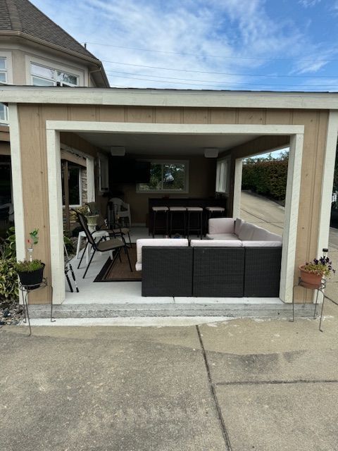 Covered patio with dark wicker seating and a grill, opening onto a driveway.