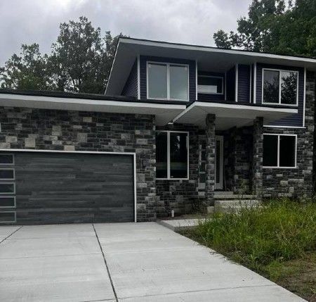 Modern two-story house with dark stone exterior, black garage door, and concrete driveway.