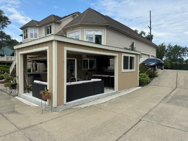 Two-story beige house with a covered patio and concrete driveway on a sunny day