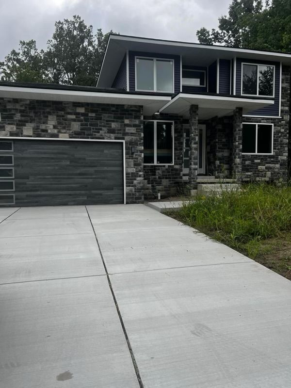Modern two-story dark stone house with a garage and concrete driveway