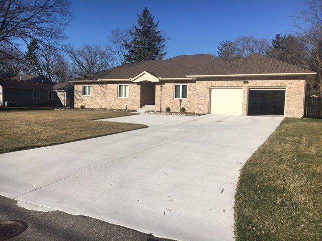 Single-story brick house with a wide concrete driveway and attached garage under a clear blue sky