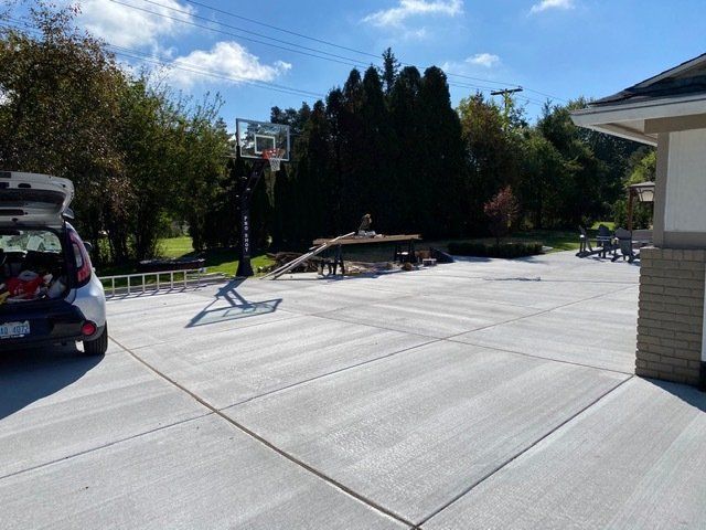 Backyard driveway with a portable basketball hoop, parked SUV, and picnic table on a sunny day