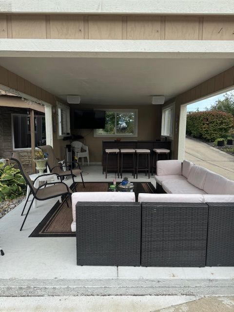 Covered patio with wicker seating, sectional sofa, and dining table overlooking a yard.