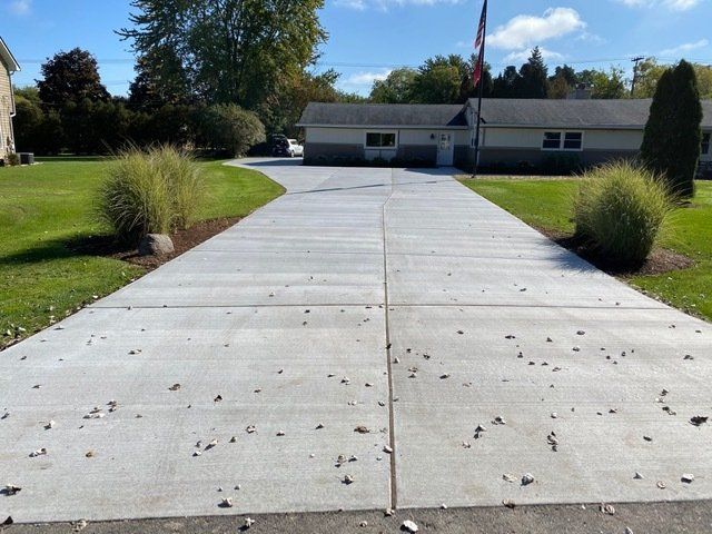 Concrete driveway leading to a low building with an American flag, flanked by grass and shrubs