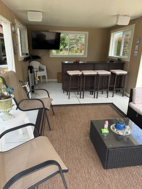 Sunroom with dining table, chairs, wall-mounted TV, and wicker seating on a woven rug.