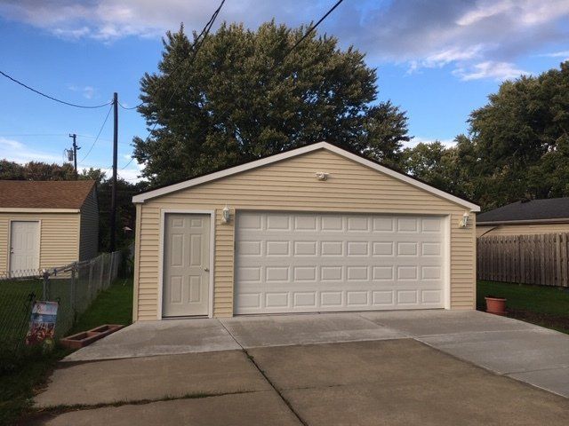 Single-car garage with beige siding and white door, front concrete driveway, under a blue cloudy sky