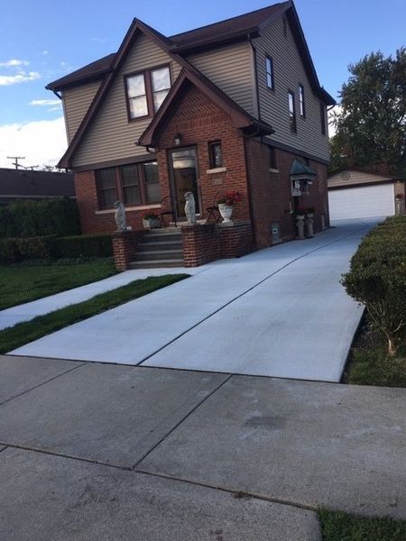 Brick house with a newly poured concrete driveway and a detached garage at the end.