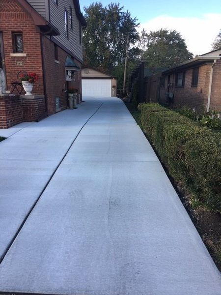 Concrete driveway between brick houses with a garage at the end and hedges along the side