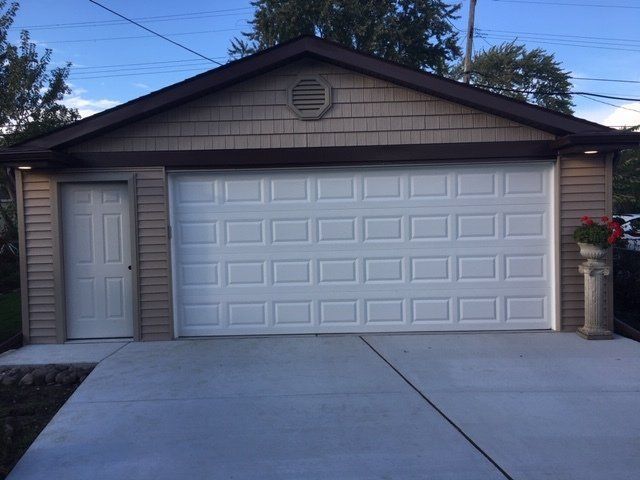 Single-story garage with white double doors, side entry door, and concrete driveway at dusk