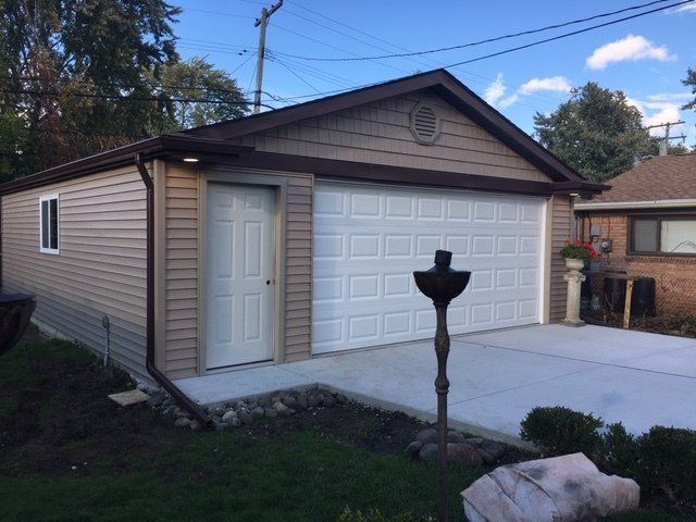 Single-car garage with beige siding, white door, and concrete driveway in a suburban yard.