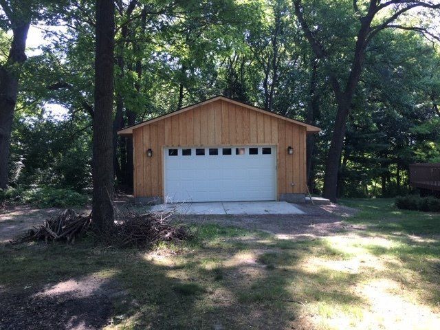 Wooden garage with white door under tall trees in a wooded yard