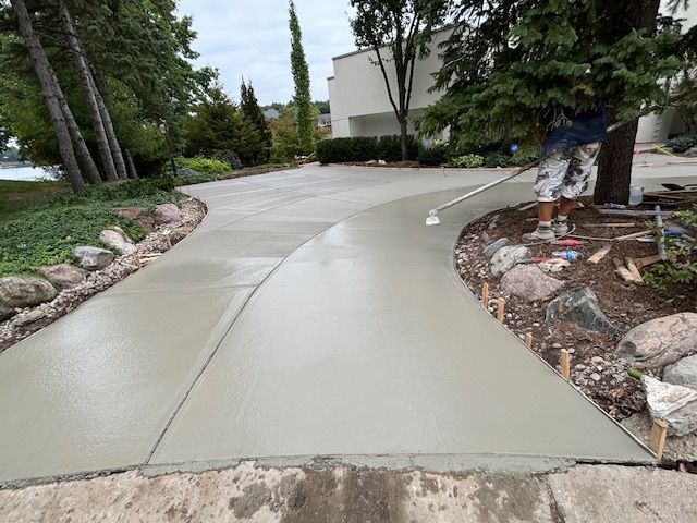 Freshly poured concrete driveway curving through a landscaped yard with rocks and trees