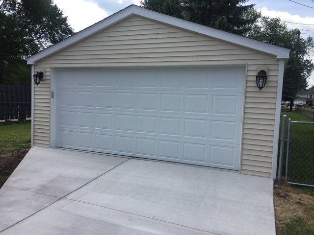 Detached beige garage with white double doors and a concrete driveway