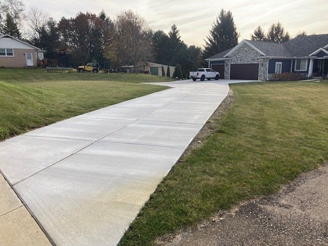 Fresh concrete driveway leading to a house with garage, bordered by green lawns on a cloudy day