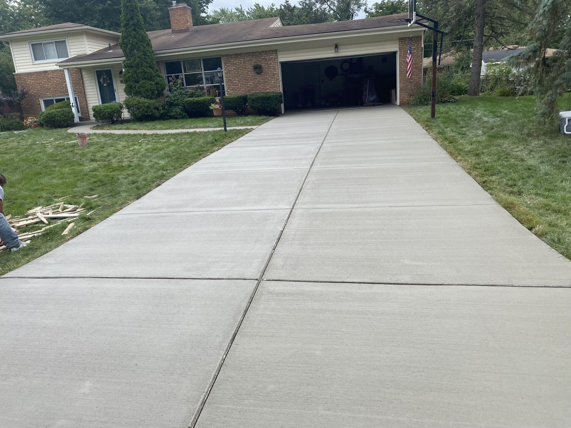 Concrete driveway leading to a brick house with an open garage and green lawn on both sides