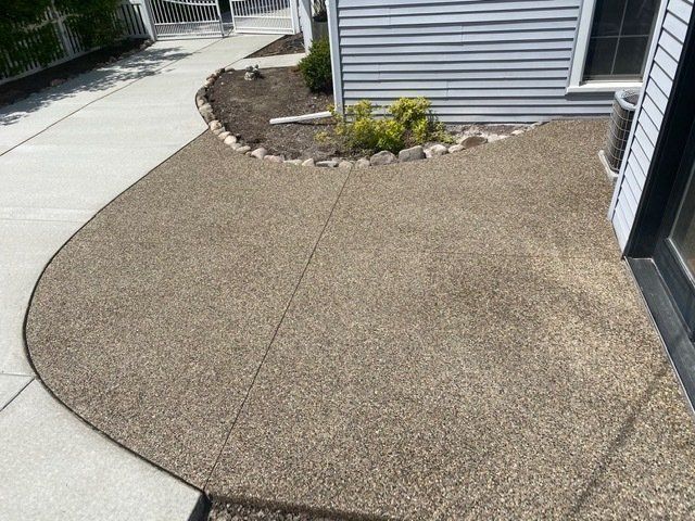Curved concrete walkway beside a house with a gravel patio and small landscaped bed