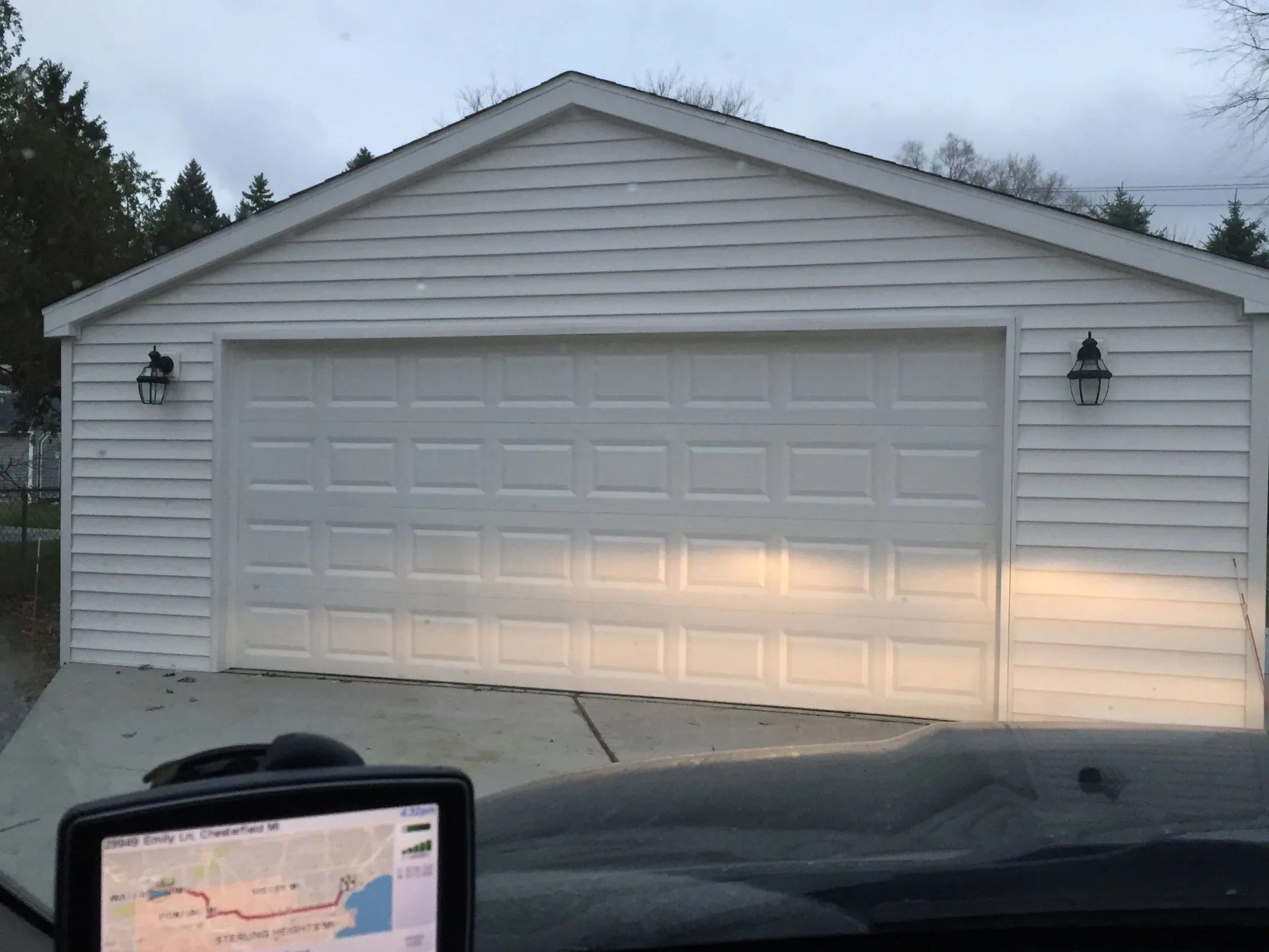 White garage with two wall lights, viewed from a car dashboard at dusk.