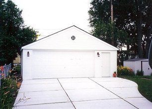 White two-car garage with double doors and a concrete driveway, framed by trees and a small side yard